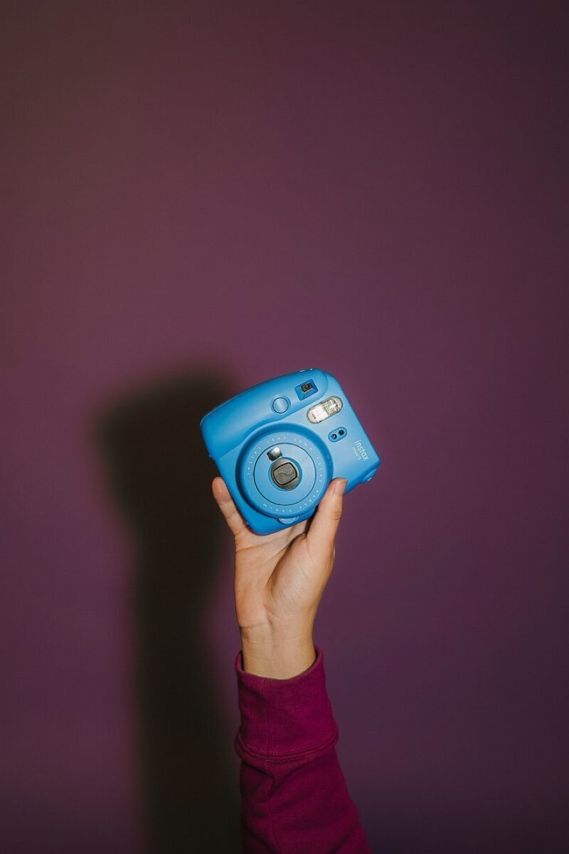 Blue polaroid being held up in front of a purple background.