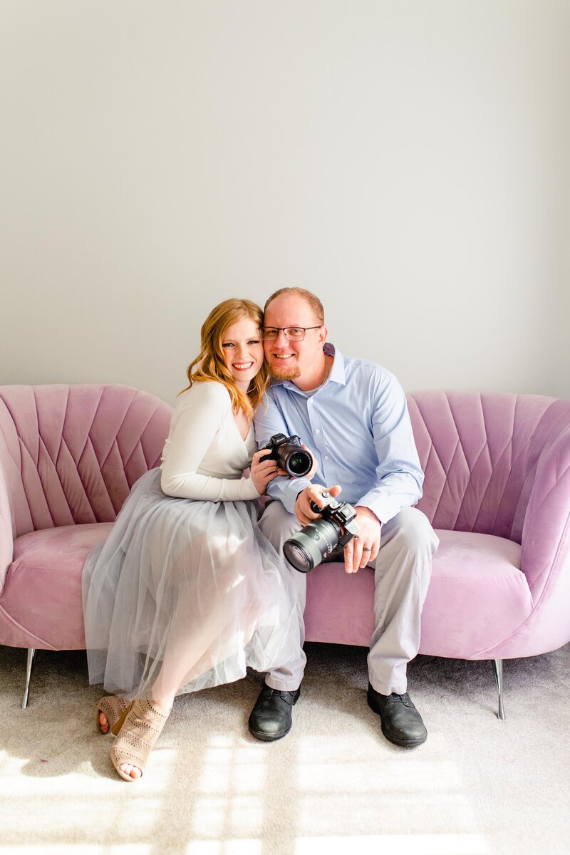 Wedding photographers holding cameras together in purple home office