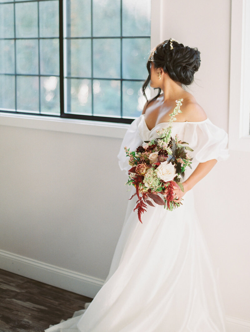 Bride wears braided bun and looks away from camera holding bold floral bouquet