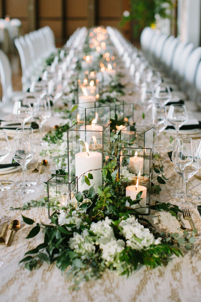 Green and white flowers with black iron and glass candle holders at head table of wedding reception with gold linens.