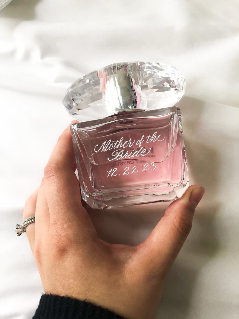 hand holding a pink perfume bottle with silver engraving