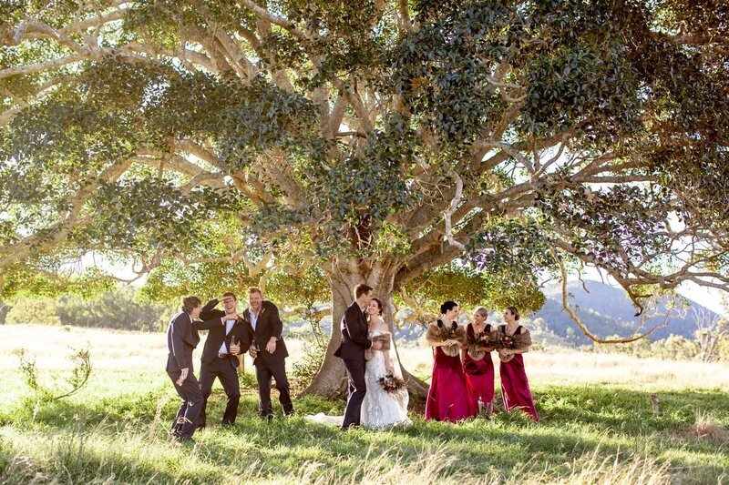 Fun wedding couple with groomsmen and bridesmaid under a big tree
