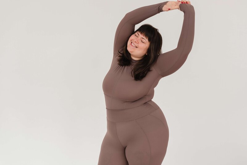 Woman in brown workout clothes stretching and smiling