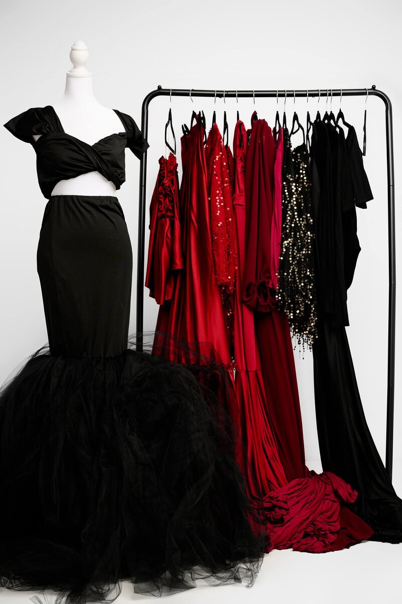 A rack of Studio maternity dresses and black and red and one highlight dress on a mannequin that's black with a tulle bottom