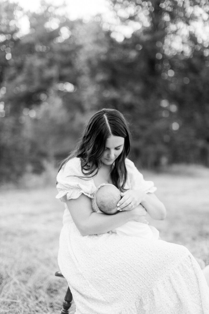 Black and white image of a mother nursing her newborn in a field