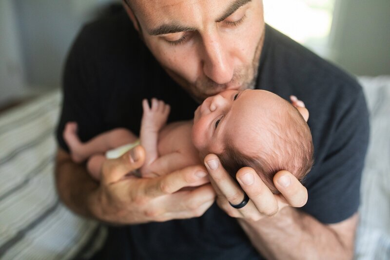 Photo of father holding newborn baby and giving kiss