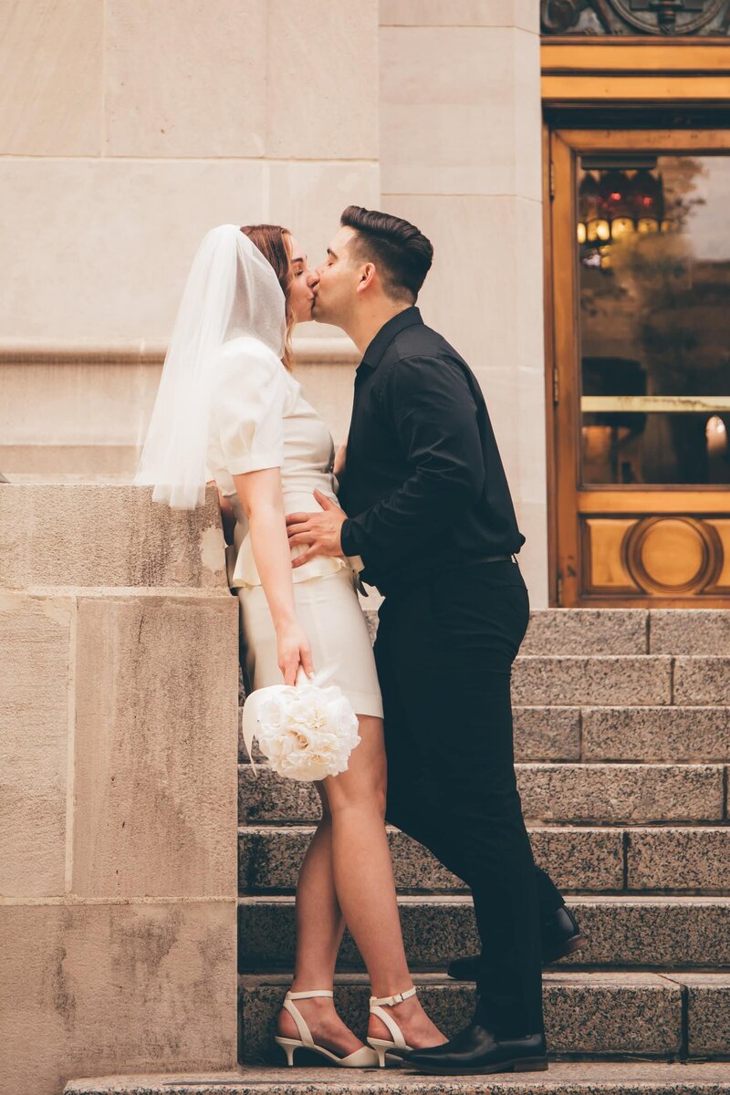 A bride and groom share a romantic kiss on the steps of a building, captured by Britt Elizabeth destination wedding photographer