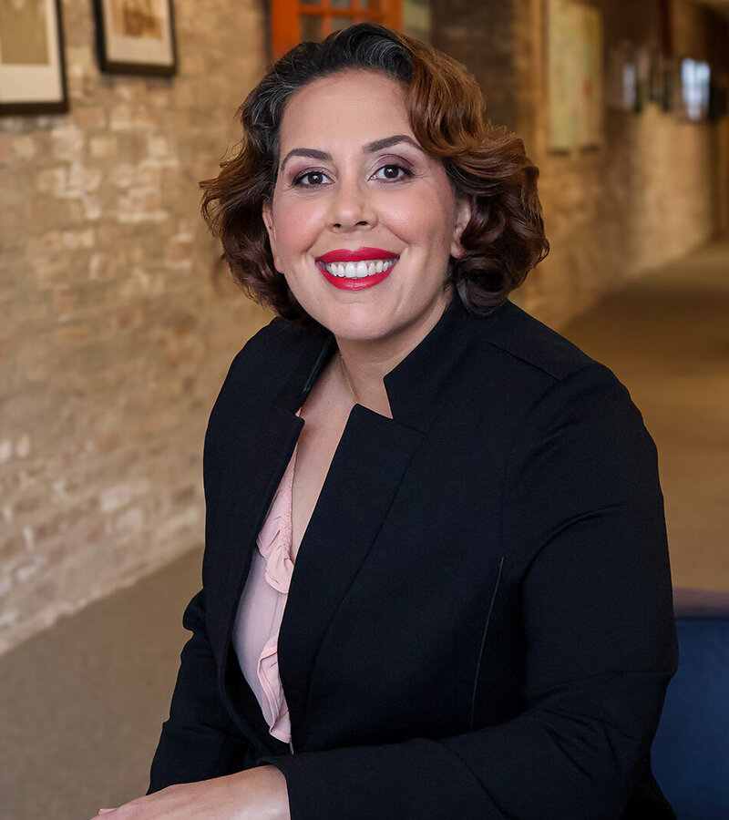 A professional portrait of Ida Salusky in a black blazer and shirt, exuding a polished and sophisticated appearance.