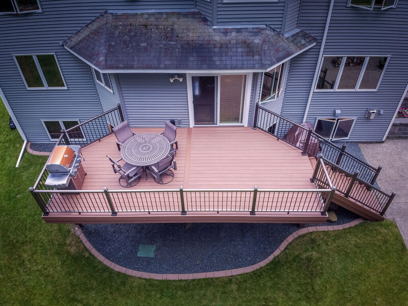 Aerial view of a composite deck using TimberTech Advanced PVC, cantilevered over a wood frame and accented with aluminum picket railing around the perimeter and down the stairs. 