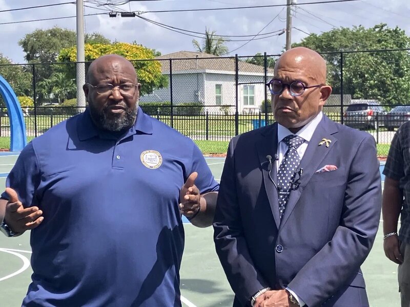 Attorney Richard Ryles standing with another African-American man on a basketball court being interviewed by reporters