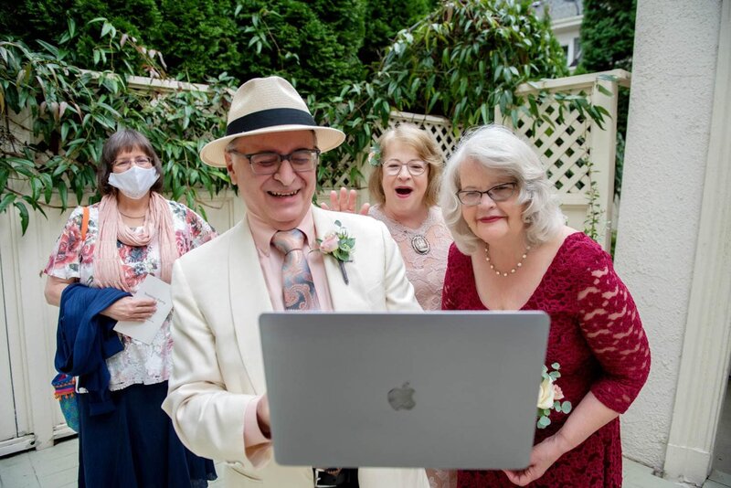an older couple looks excitedly on the apple computer to talk to guests who joined their wedding via zoom
