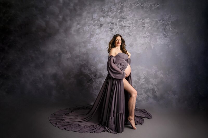 dusty purple dress  on purple background while mom cradles her baby bump with belly extended