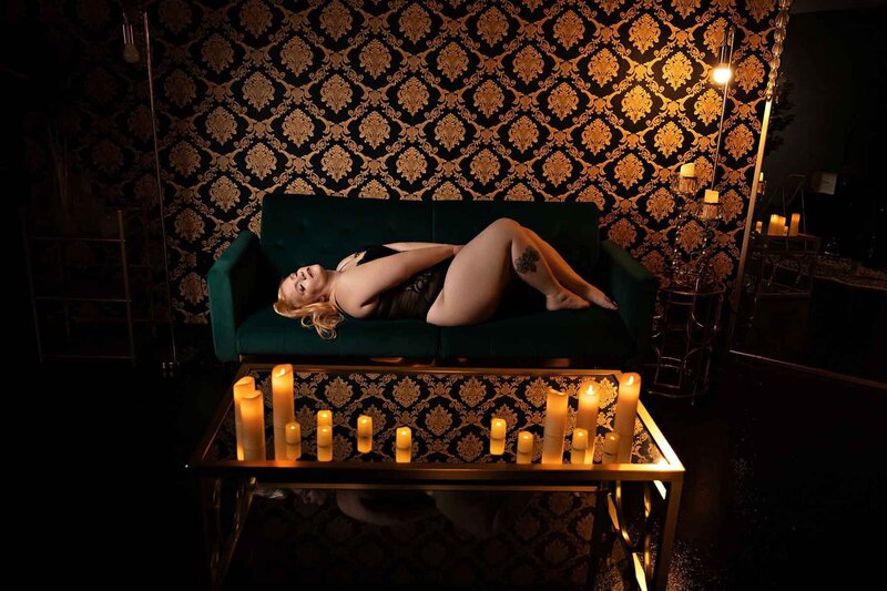 Red haired woman laying on emerald green couch infront of black and gold baroque backdrop