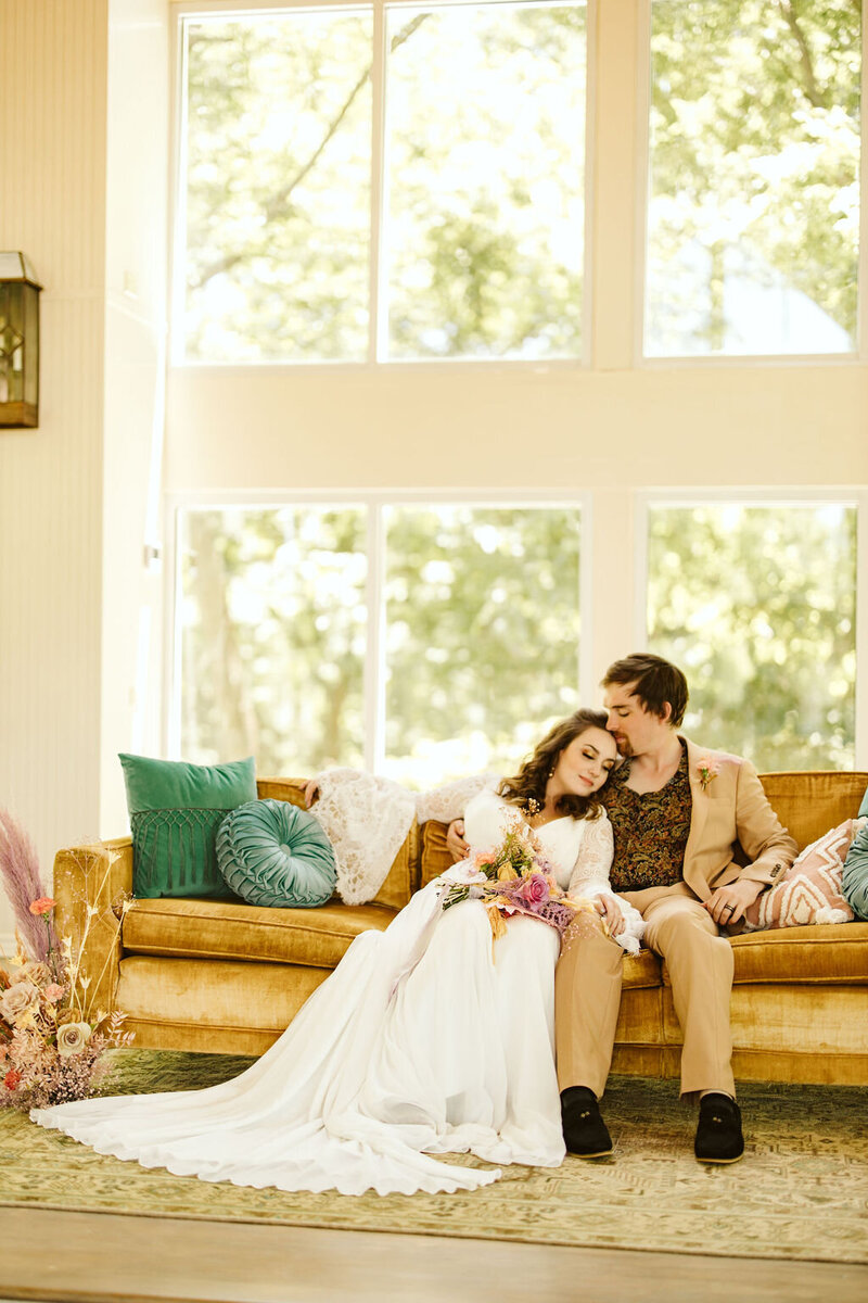 bride leans on groom's shoulder on a mustard velvet couch