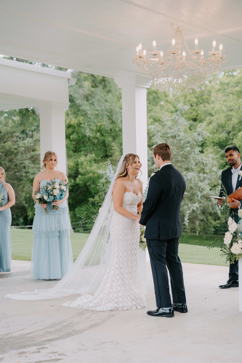 Outdoor wedding ceremony under a white pavilion with a chandelier, where the bride and groom exchange vows