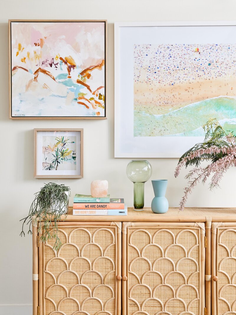 A rattan side board with a colourful picture gallery wall art layout with plants, vases and books on the sideboard