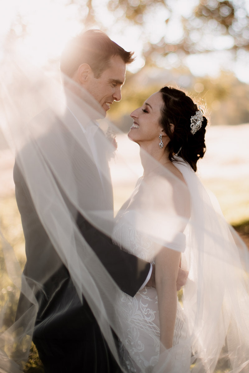 Bride and Groom smiling at each other covered  in the shadow of a veil