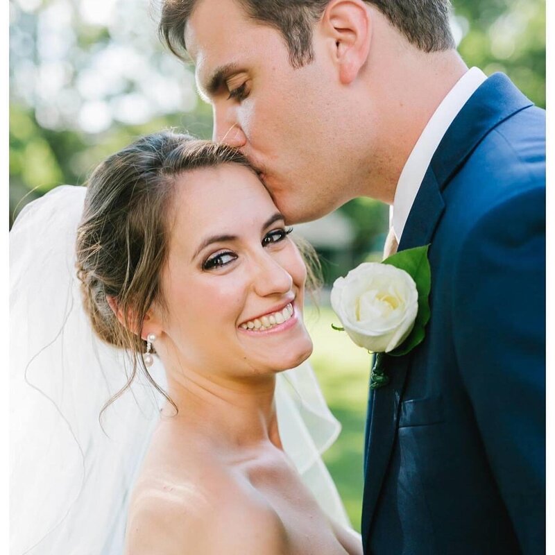 bridal hair and makeup and groom kissing her forehead
