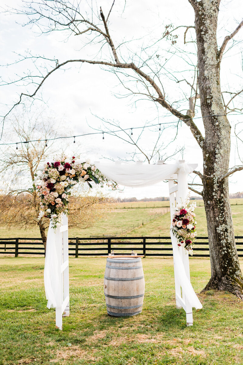 outdoor wedding ceremony decor with an arch covered in white draping and decorated with lush florals