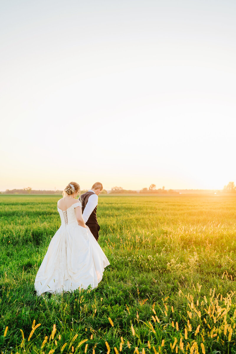 A Wisconsin newly married couple walking in a field towards a golden sunset.