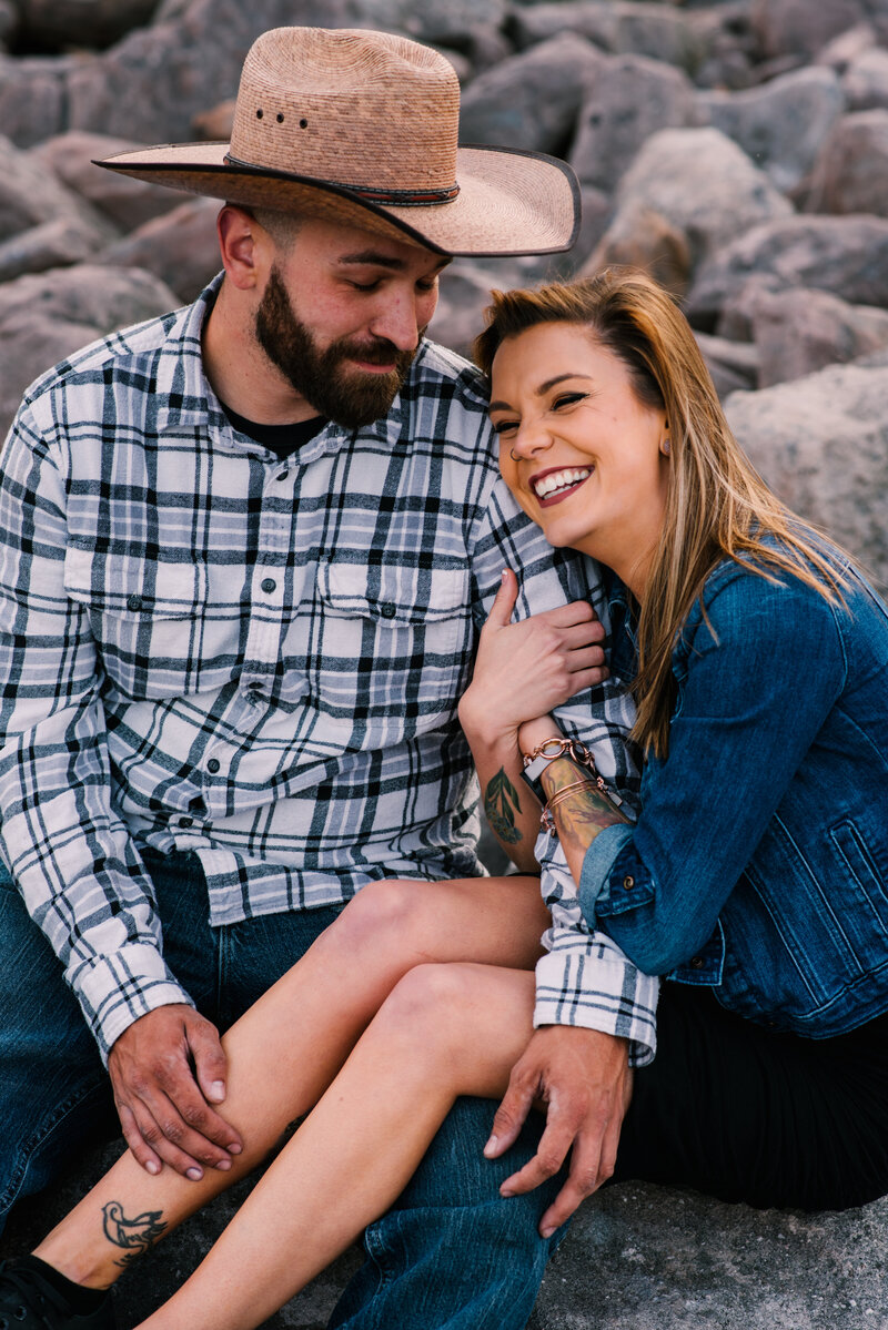 Couple poses on rocky shore for engagement session.