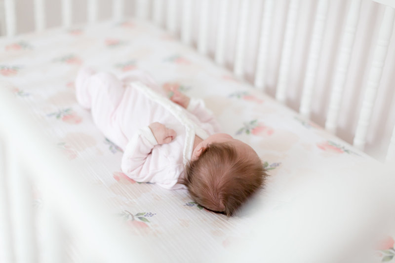 newborn baby girl sleeps in her neutral white crib