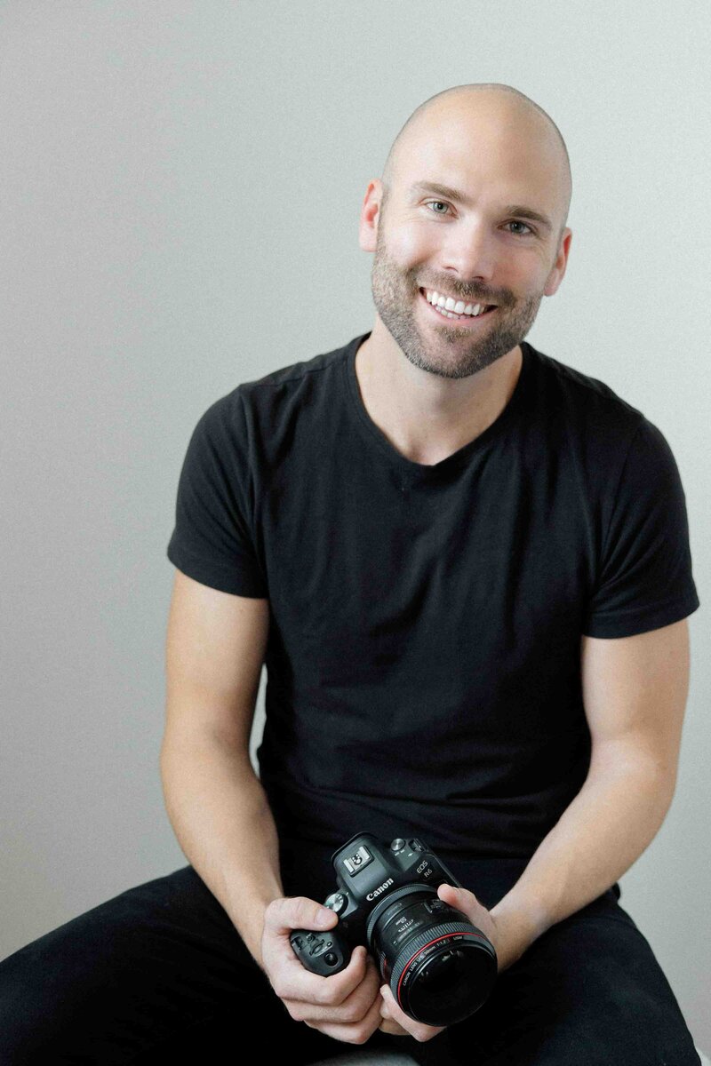 Photo of Andrew posing with his camera and smiling
