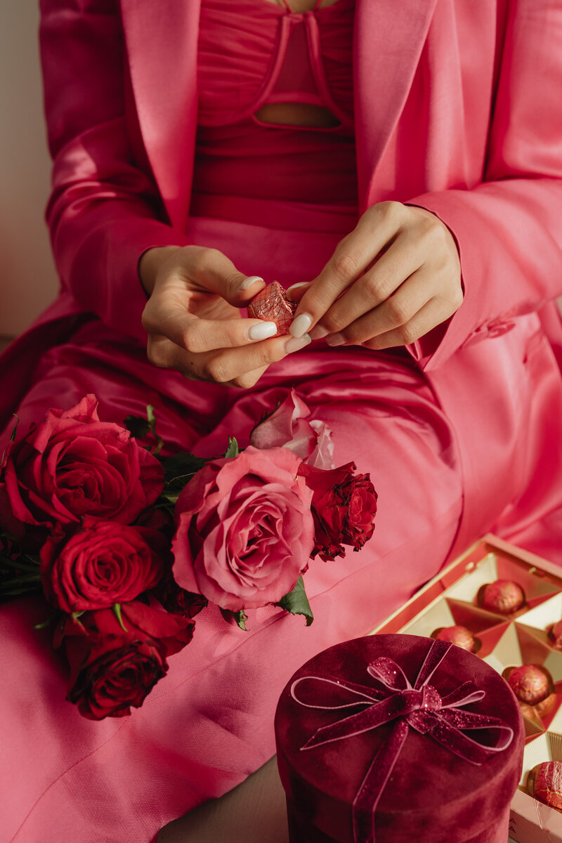 Creative branding photo featuring pink styling, roses, and chocolates with hands unwrapping a sweet.