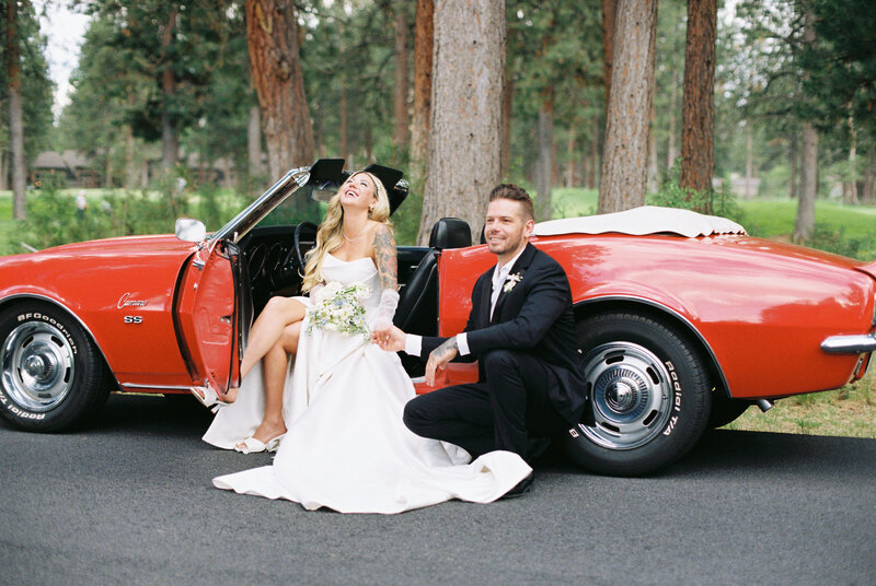 Wedding couple in classic red car, laughing.