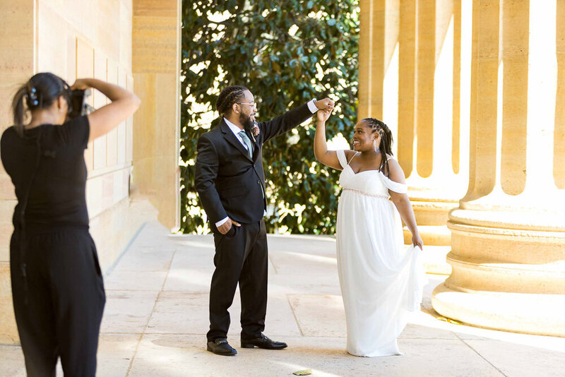 behind the scenes with black Wedding photographer with a black young wedding couple on the step of a museum. The couple is dancing.