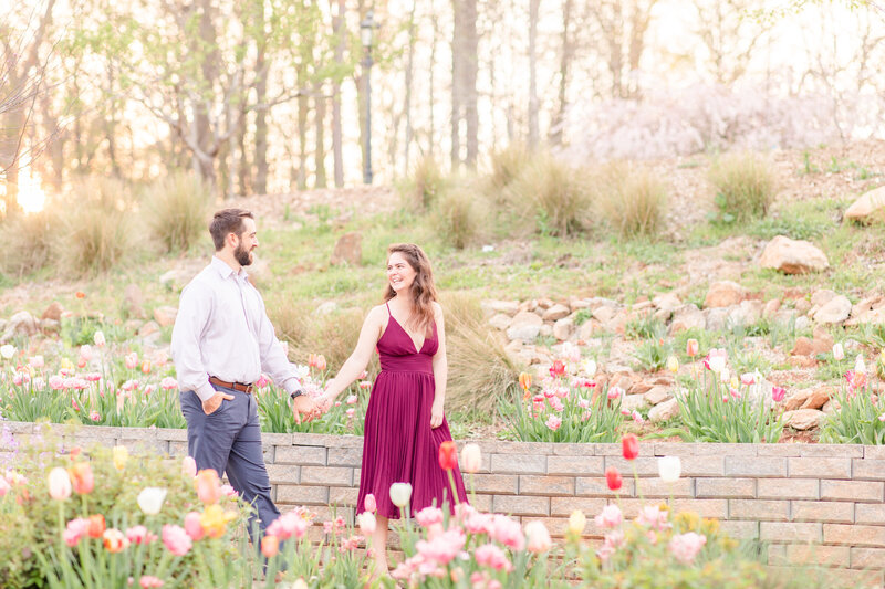 A couple holds hands as they walk through flowers and tulips in the spring at the State Botanical Gardens of Georgia in Athens for their engagement session.