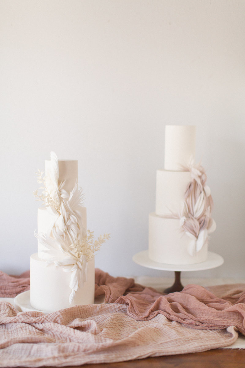 Two beautiful three-tiered wedding cakes on display on top of mauve colored gauze