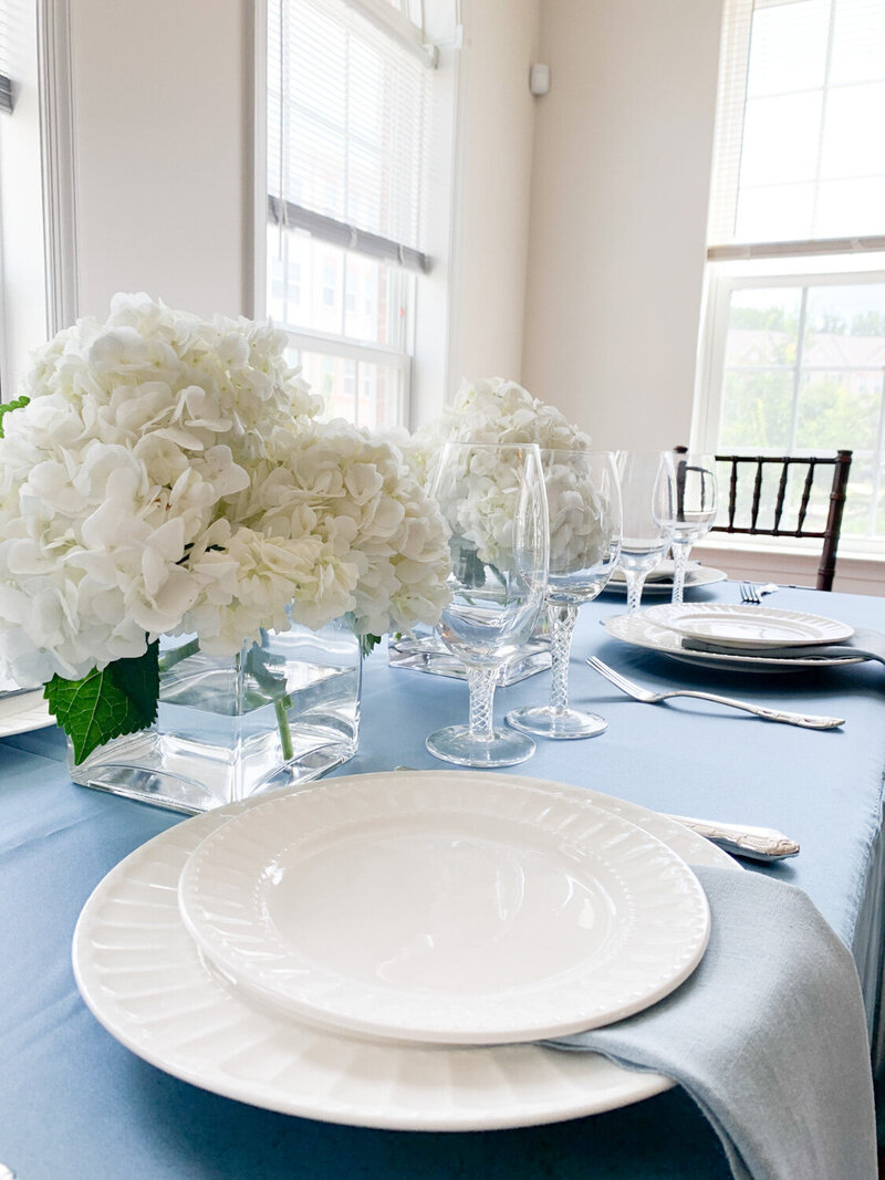 White floral centerpiece, glasses, plates, and utensils on top of the table