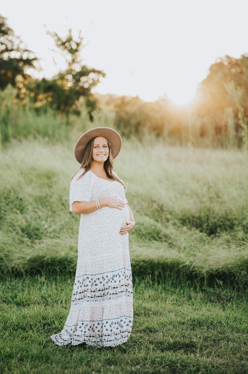 Pregnant woman smiles at camera with hands on belly during maternity session in Raleigh NC