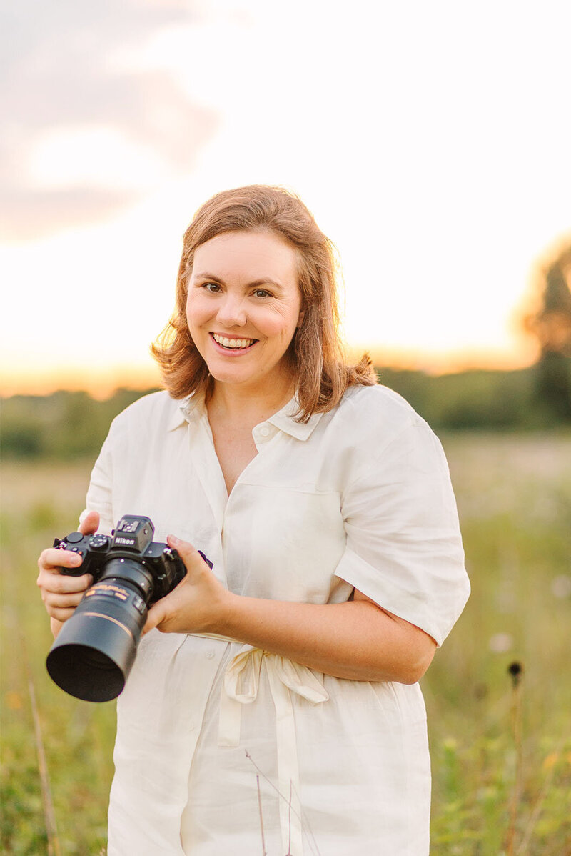 Chicago senior photographer Kristen Hazelton wearing a white dress in a field and holding a camera