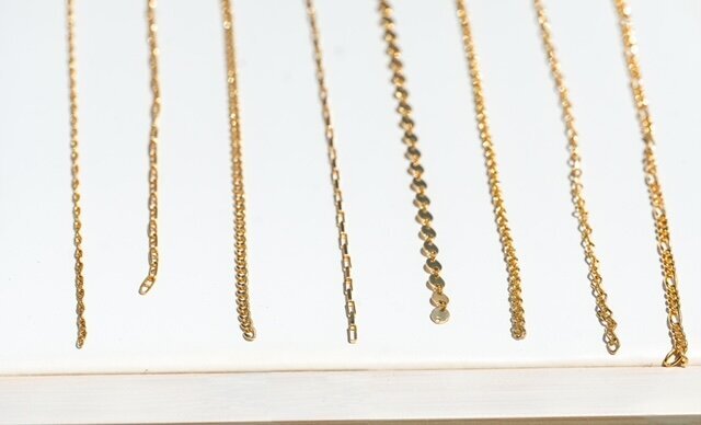 Close-up of gold-filled chain samples in various styles displayed on a white jewelry board.
