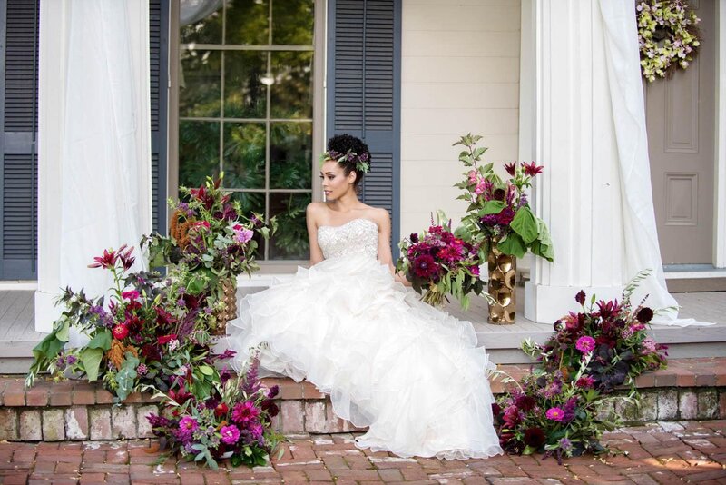 a bride sits on a stoop surrounded by purple and pink flowers
