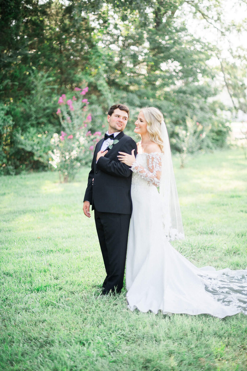 bride and groom look at one another in grassy area at legacy acres by arkansas wedding photographer
