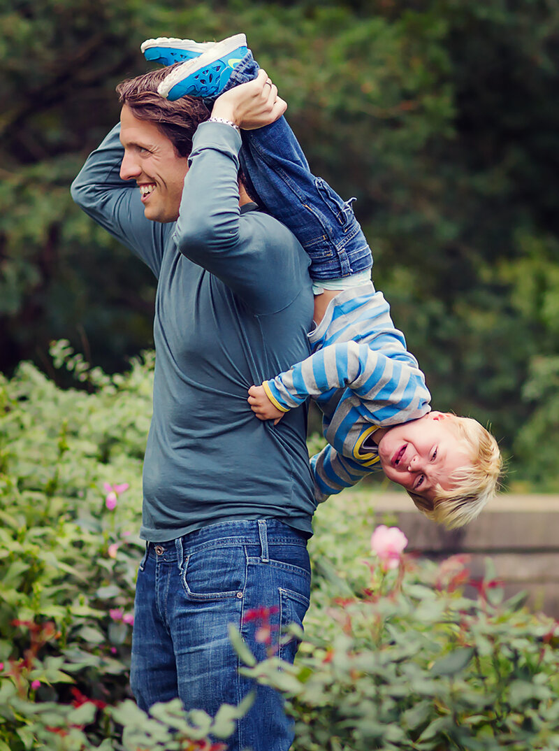 Dad and his toddler at at the Newfields Gardens in Indy. Dad is smiling and holding his son upside-down behind him, who is crying.