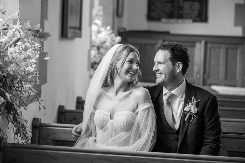 Intimate moment: Newlyweds sitting on church pews, in black and white.