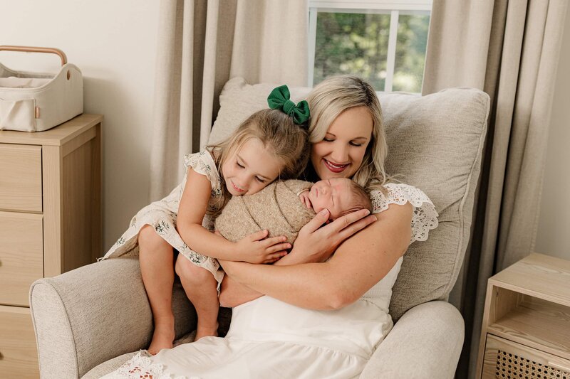 mother holds her newborn baby boy wrapped in brown while her daughter sits beside her