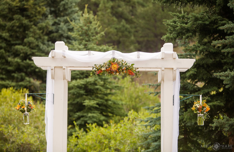 Detail of the white wood wedding arbor with orange florals at Mountain View Ranch