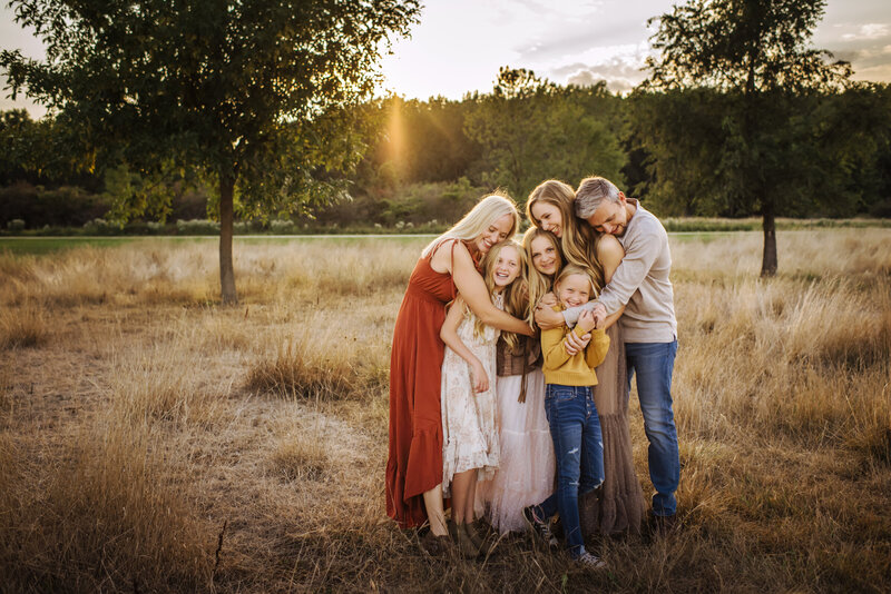 Mom and dad with 4 daughters standing in between them hugging them