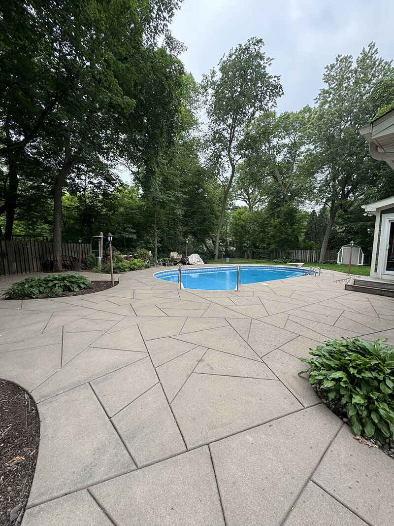Stamped concrete with curved edges and an in-ground pool in the background. 
