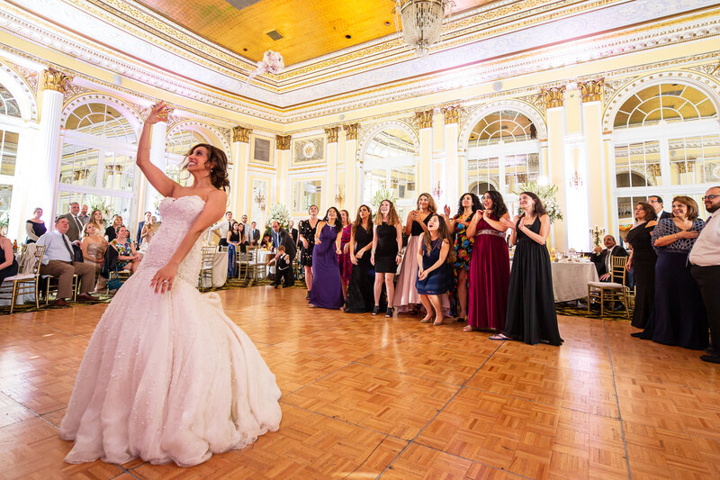 Bride tossing a bouquet at a wedding and flowers are still in the air in a luxury banquet hall.