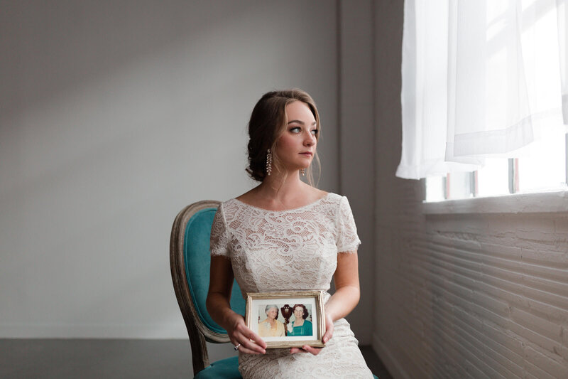 bride holds a photo of her grandmothers as she looks out a window during her engagement session at The Creative Chateauin Houston by Swish and Click Photography