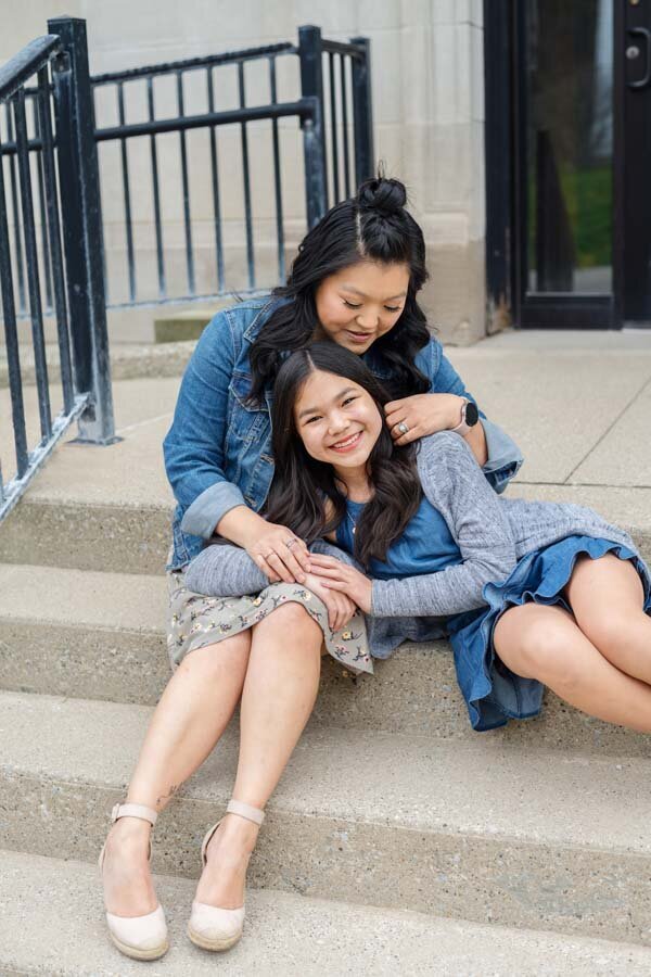 Two women in denim jackets smiling and sitting closely together on outdoor steps.