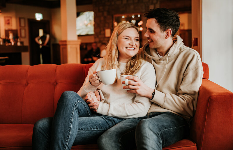 Man and woman having a coffee cuddle on sofa during pre wedding shoot in glencoe scotland