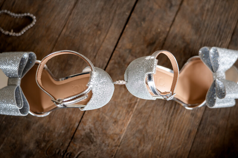 Silver wedding heels displayed creatively on wooden table – photographed by wedding photographer Niko Coric – Lumen Clarity Media