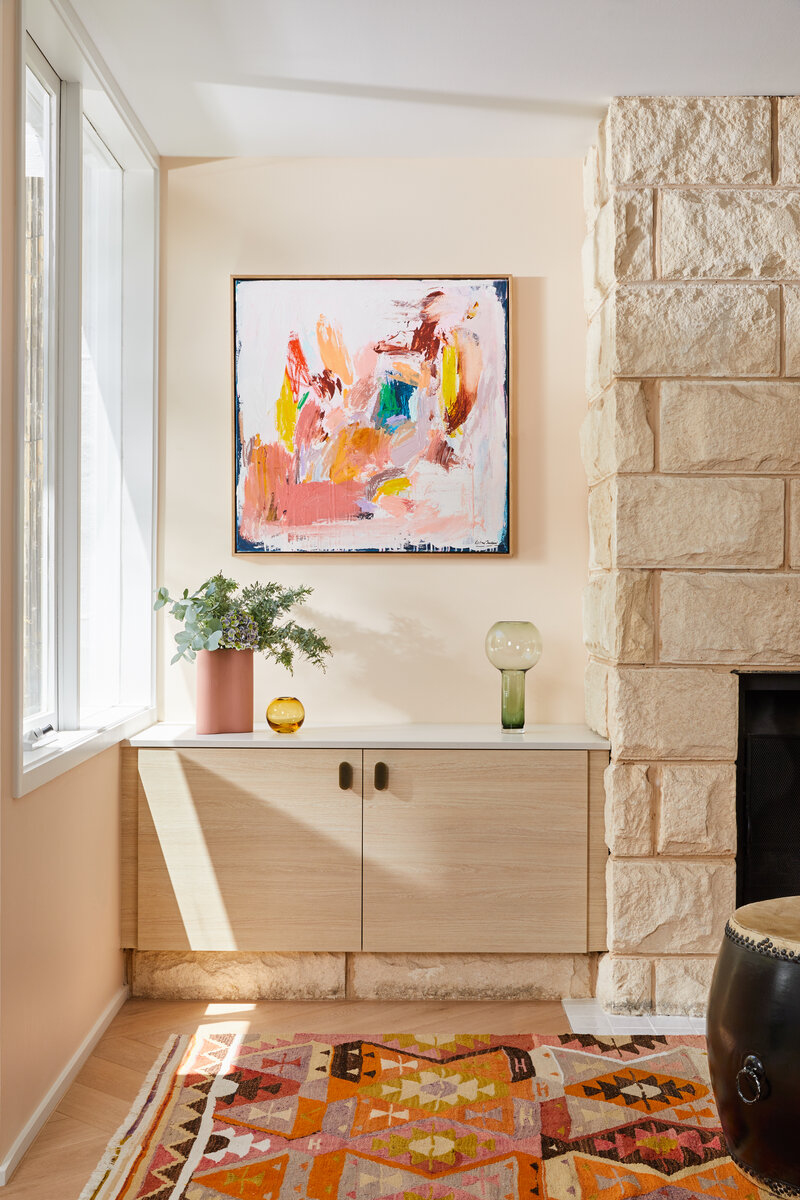 Modern living room corner styled by Melbourne interior stylist Lisa Hunter, featuring colourful abstract artwork, timber cabinetry, and natural stone wall.